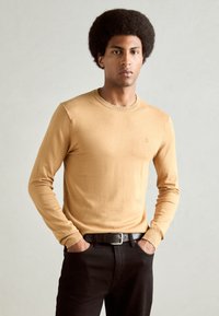 Long-sleeve yellow sweater made of knit fabric, featuring a crew neck and ribbed cuffs. Worn with black pants and a black belt.