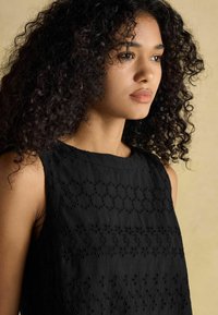 Melna bez piedurknēm topa augšdaļa ar teksturētu ziedu izšuvumu, apaļu kakla izgriezumu un pieguļošu siluetu, izceļot sarežģīto rakstu.