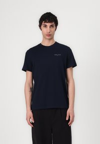 T-shirt en coton bleu marine à manches courtes et col rond, avec un petit logo blanc "TOMMY JEANS" sur le haut à gauche de la poitrine.