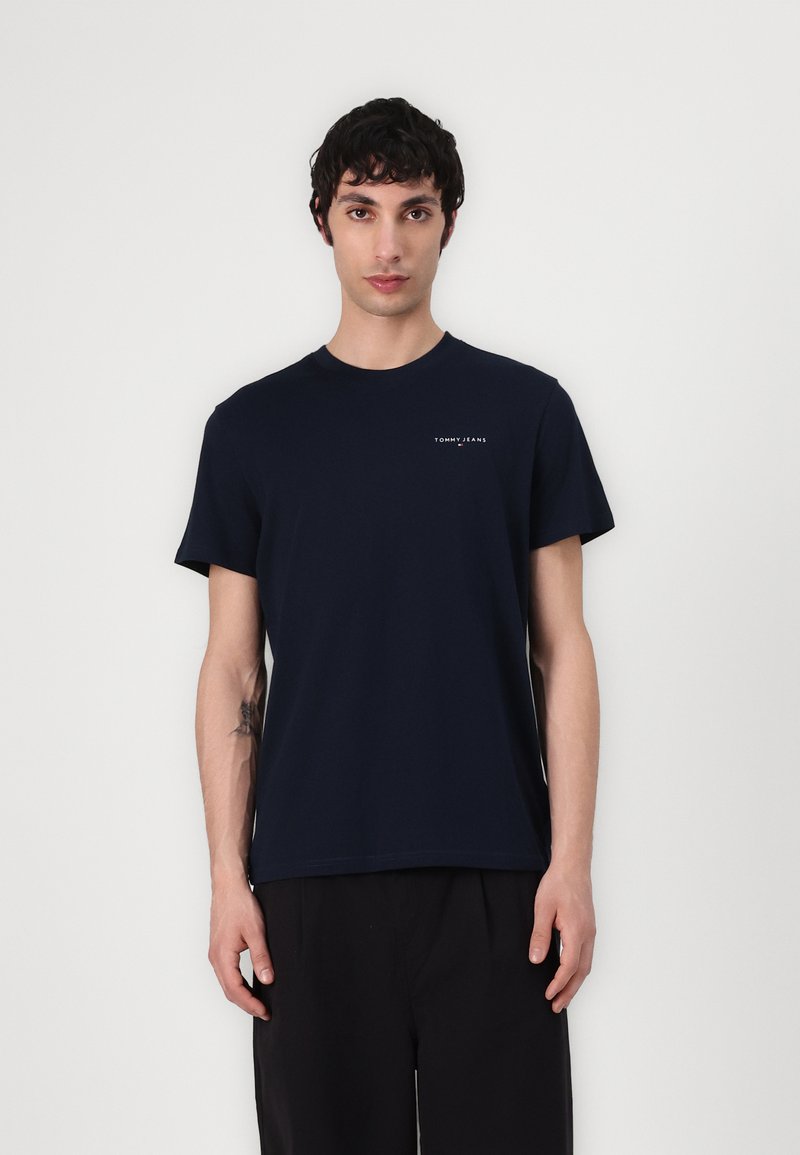 T-shirt en coton bleu marine à manches courtes et col rond, avec un petit logo blanc "TOMMY JEANS" sur le haut à gauche de la poitrine.