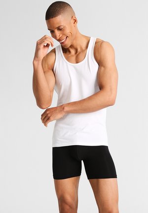 Weißes Baumwolltanktop kombiniert mit schwarzer dehnbarer Unterwäsche, körperbetontes Design, glatte Textur, das den Oberkörper und die Arme präsentiert.