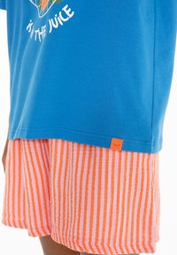 Modré tričko s grafickým textem a šortky s oranžovými pruhy, které jsou nošeny na dolní části těla a horních nohách osoby.