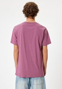 T-shirt a maniche corte in un delicato color malva, realizzato in morbido cotone. Presenta un collo rotondo e una vestibilità rilassata; il retro è semplice con un orlo leggermente abbassato.
