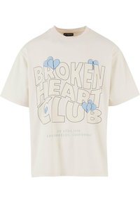 Krém színű pamut póló kerek nyakkal, amelyen feltűnő fekete szöveg olvasható: "BROKEN HEART CLUB", valamint kék szív grafika található az elején.