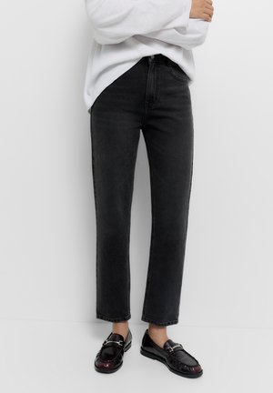 Crne traperice s ravnim nogavicama, visokim strukom i dizajnom od pet džepova, uparene s sjajnimm crnim mokasinkama. Teksturirani materijal.