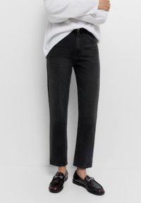 Zwarte denim jeans met een recht gesneden pijp, hoge taille en vijf zakken, gecombineerd met glanzende zwarte instappers. Gestructureerde stof.