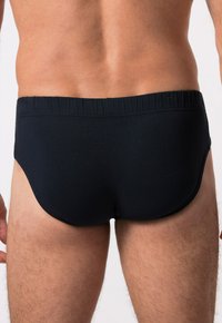 Slip da bagno neri con una texture liscia, cintura elastica e un design aderente, mostrati da dietro, evidenziando la parte bassa della schiena e le cosce.
