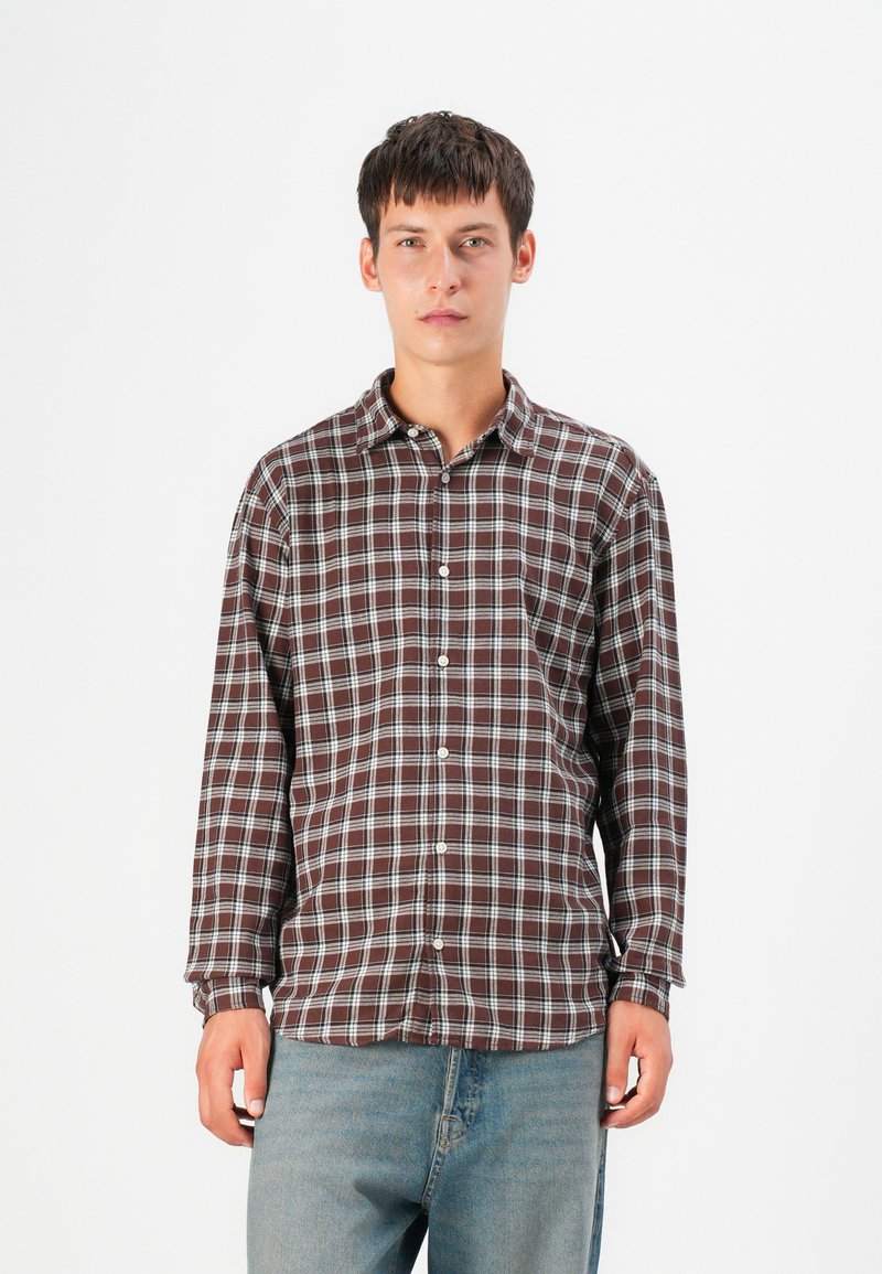Brown and blue checkered long-sleeve shirt with a button-down collar and front pocket, made of a lightweight fabric, worn over denim jeans.
