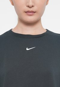 Tumši pelēks džemperis ar apaļu kakla izgriezumu, kam ir balts Nike logotips izšūts krūtīs. Gluda auduma tekstūra.