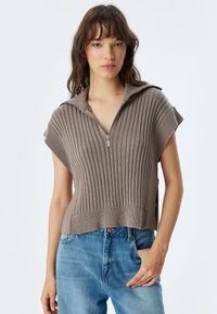 Braunes, geripptes Kurzarmpullover mit Reißverschluss und breitem Kragen, kombiniert mit hochgeschnittenen blauen Jeans. Glatte Textur, lässige Passform.