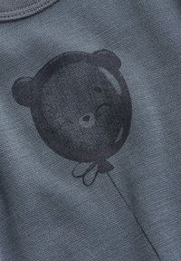 Blauwe stof met een gestructureerde weving, voorzien van een donkere ballon in de vorm van een beer. Het ontwerp bevat vage gelaatsdetails en een vastgebonden uiteinde.