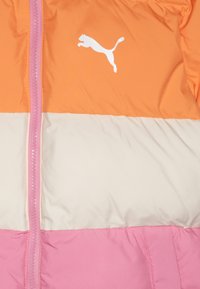 Puma striukė su oranžiniais, grietinėlės ir rausvais spalvų blokais. Yra baltas logotipas, pilnas užtrauktukas ir lygus, blizgus audinio paviršius.