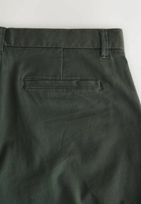 Dark green pants featuring a smooth texture and a single back pocket, with a straight waistband and belt loops.