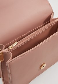 Růžová kožená kabelka s kapsou na zip a magnetickým uzávěrem. Hladký povrch s akcenty zlaté kovový. 