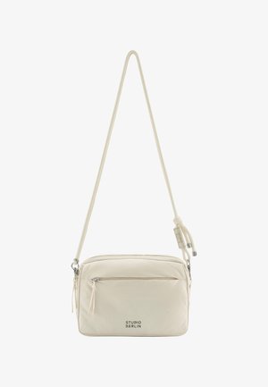 Rechteckige Umhängetasche in cremefarbe mit vorderer Reißverschlusstasche, verstellbarem Riemen und "STUDIO BERLIN"-Logo vorne.