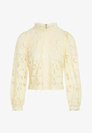 Blouse en dentelle crème à manches longues avec col montant, bords festonnés, motifs floraux découpés complexes et fermeture éclair au dos.