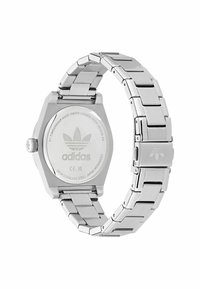 Montre en acier inoxydable argenté avec un boîtier octogonal, un bracelet en métal et un logo Adidas gravé au dos. Présente une surface texturée.