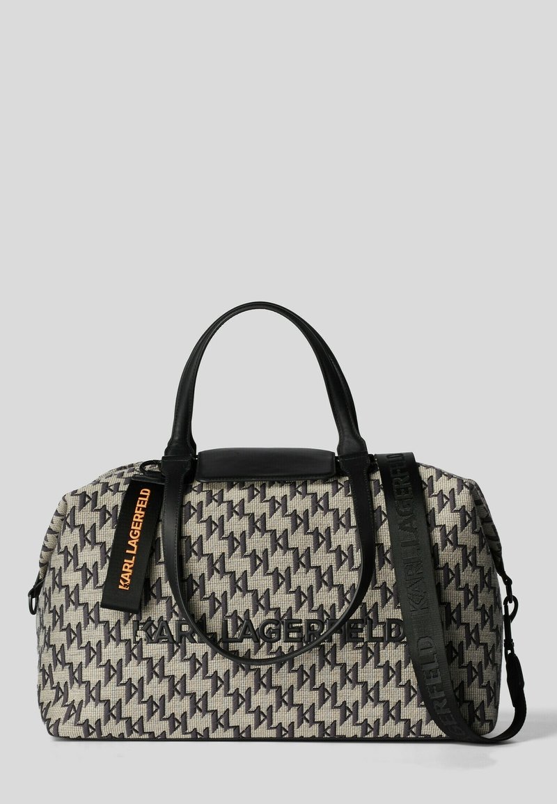 Sac en tissu noir et beige avec un motif de logo répétitif, poignées doubles, une bandoulière amovible et un accent noir lisse sur le dessus.