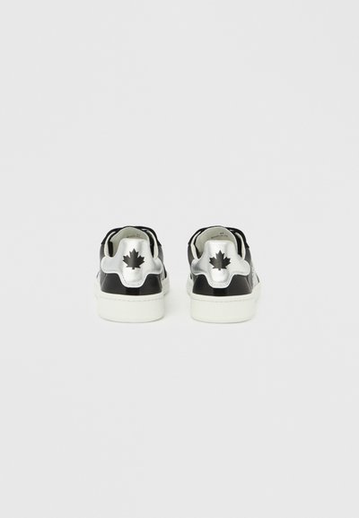 Baskets noires et argentées à finition brillante, avec un accent en forme de feuille d'érable, semelle blanche et design à bout arrondi. Apparence simple et moderne.