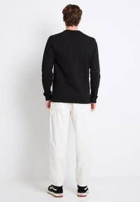 Czarny sweatshirt z długimi rękawami, ściągaczami na rękawach i na dole, w połączeniu z luźnymi białymi spodniami i czarnymi sneakersami z białym logo.