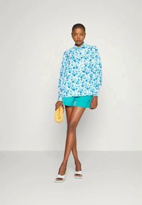 Blusa com padrão floral azul combinada com calções turquesa. Os acessórios incluem uma bolsa amarela e sandálias brancas. Tecido liso com design ajustado.