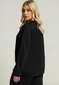 Sudadera de forro polar negra con mangas largas, un corte holgado y puños acanalados. Presenta un cuello redondo y una textura suave.