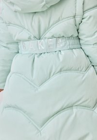 Zelena puffer jakna s chevron šavovima, elastična struk s natpisom "BAKER" i glatka, sjajna tekstura.