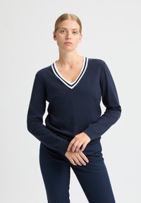 Marineblauwe trui met een V-hals en wit gestreepte afwerking. Lange mouwen en geribbelde manchetten. Zachte stof met een aangesloten pasvorm en minimale details.