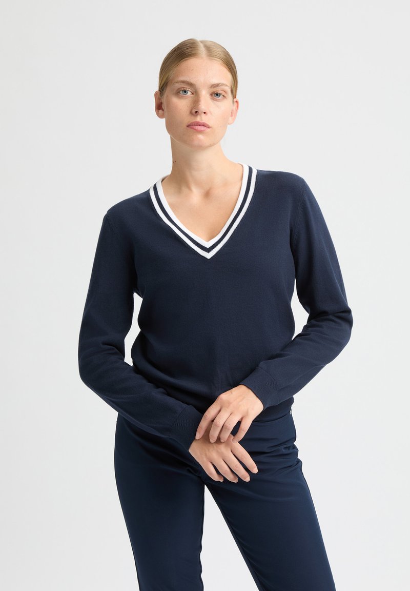 Marineblauwe trui met een V-hals en wit gestreepte afwerking. Lange mouwen en geribbelde manchetten. Zachte stof met een aangesloten pasvorm en minimale details.