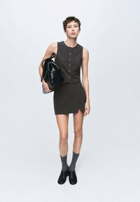 Conjunto de dos piezas gris que incluye una blusa sin mangas con botones y una falda mini ajustada. Combinado con botines negros y calcetas grises.