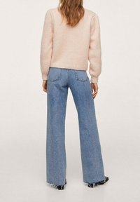 Jasnoróżowy, gruby sweter z dzianiny w połączeniu z niebieskimi, szerokimi dżinsami z wysokim stanem, z postrzępionym dołem i subtelnym przeszyciem na tylnych kieszeniach.