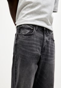 Grå denimjeans med en lige benpasform, der har subtil falming, syede lommer og metalbeslag ved taljen.