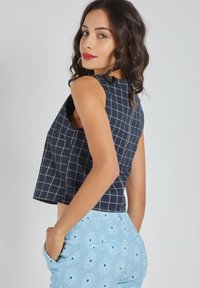 Top corto de color marino con un patrón de cuadrícula, combinado con pantalones celestes adornados con margaritas blancas y azules. Textura de tela suave, diseño sin mangas.