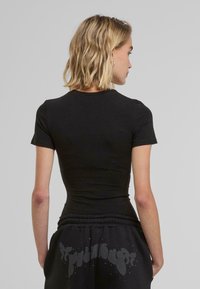 Svart kortärmad t-shirt med en figursydd passform och slät textur, med en klassisk rund halsringning. Baksidan visar enkelhet utan mönster.
