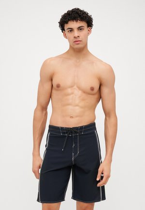 Schwarze Badeshorts mit weißem Nähen, elastischem Bund und Kordelzug. Hergestellt aus einem glatten, leichten Material; knielange Passform.