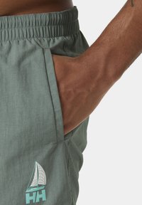 Bañador verde claro con cintura elástica, bolsillo lateral y un logo de velero en blanco y azul verdoso en la pierna.