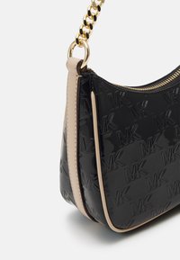 Svart lackhandväska med beige detaljer, med präglad MK-logotyp, en guldkedjeslyckta och dragkedjestängning.