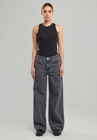 Black sleeveless tank top paired with high-waisted, wide-leg black and gray pinstriped trousers. Smooth fabric and casual fit.