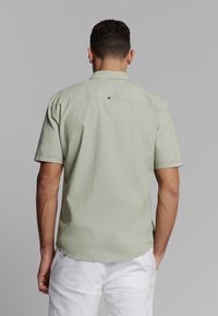 Korte mouwen, lichtgroen shirt met een rechte zoom en rugpasdetail. Gemaakt van een zachte, gestructureerde stof. Geen zichtbare patronen of accenten.