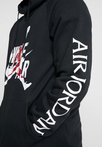 Felpa nera con cappuccio. Presenta una grande grafica bianca e rossa sulla parte anteriore e "AIR JORDAN" stampato in bianco sulla manica. Tessuto morbido.