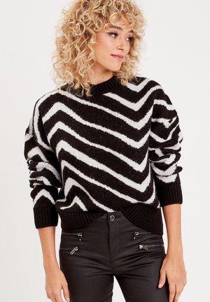 Maglione a righe zigzag bianco e nero con scollatura tonda e polsini a costine. Il materiale sembra morbido e testurizzato.