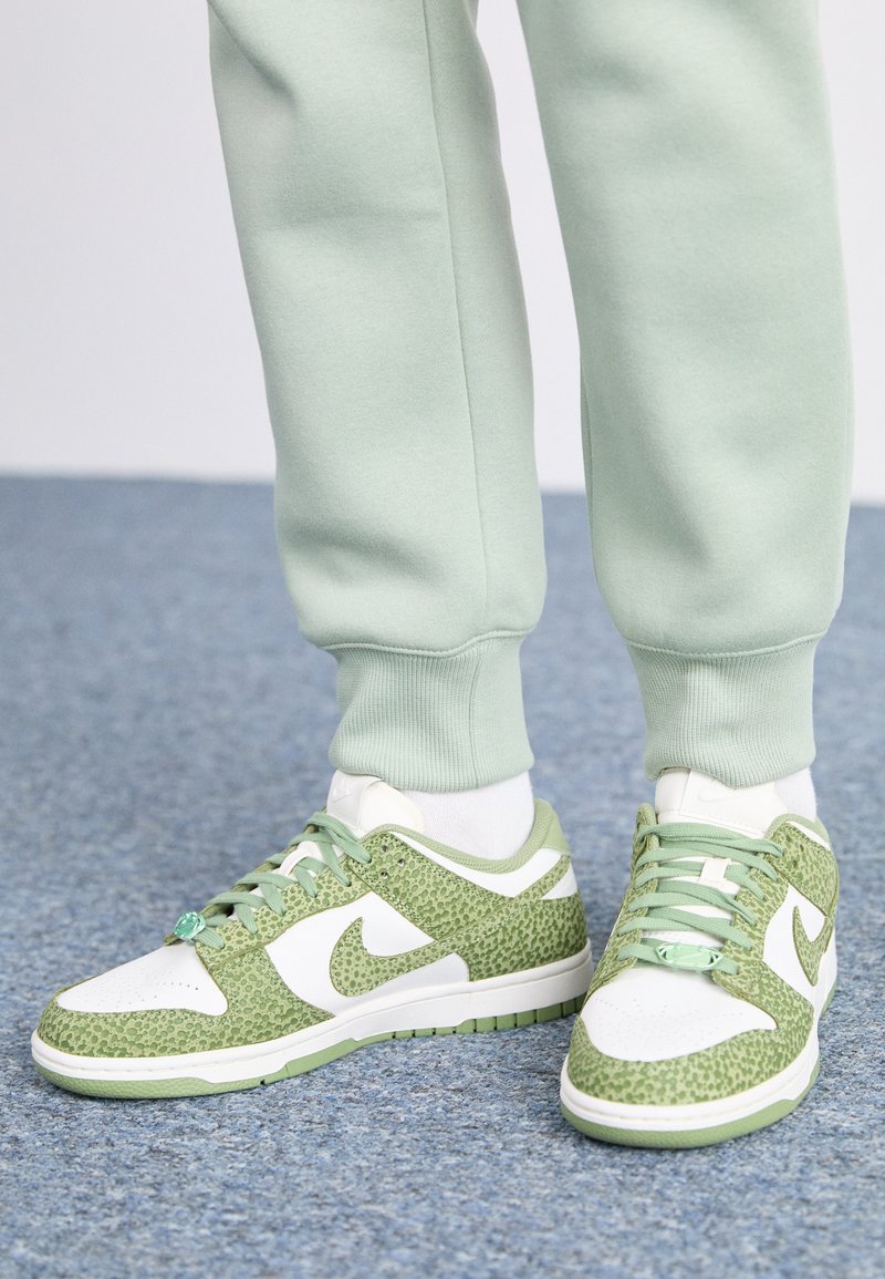 Baskets vertes et blanches avec un motif texturé, dotées d'une coque blanche et de lacets, accompagnées d'un pantalon de survêtement vert clair et de chaussettes.