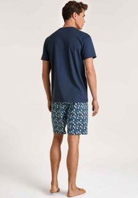 Marineblaues Baumwoll-T-Shirt mit Rundhalsausschnitt, kombiniert mit gemusterten Shorts in Blau, die weiße Blumenmuster aufweisen. Modell von hinten gezeigt.