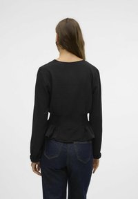 Juoda tekstūruota ilga rankovė viršūnė su apvaliu kaklu, surinkta liemens detalė ir peplum apdaila, derinama su tamsiai mėlynomis džinsinėmis kelnėmis.