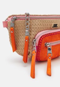 Sac banane en tissu tricoté de couleur beige avec des accents roses, comportant une poche en daim orange, des zips en argent et des pompons en tissu orange.