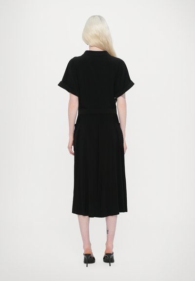 Vestido negro con mangas cortas, cintura ceñida y falda plisada. Fabricado en tejido suave, con cuello y aberturas a los lados.
