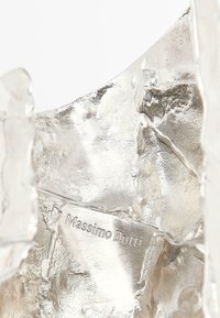 Oggetto decorativo in argento con superficie testurizzata, caratterizzato da un'incisione del logo. Il design è astratto e di forma irregolare.