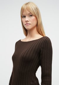 Rudas, gofruotas, glaudus marškinėlių viršus su plačia apvaliomis iškirpte ir ilgomis rankovėmis, pasižymintis minkšta tekstūra ir vertikalių dryžių raštu.