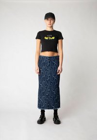 Svart kortärmad t-shirt med texten "drive"; denim maxi kjol med vågmönster och fransig nederkant. Svarta platåskor och en keps fulländar looken.