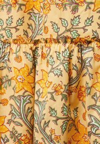 Tessuto floreale con sfondo giallo, foglie verdi e fiori arancioni, caratterizzato da una texture con cuciture arricciate per maggior dettaglio.